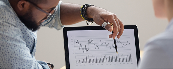 two business professionals having a discussion while looking at graphs displayed on a screen